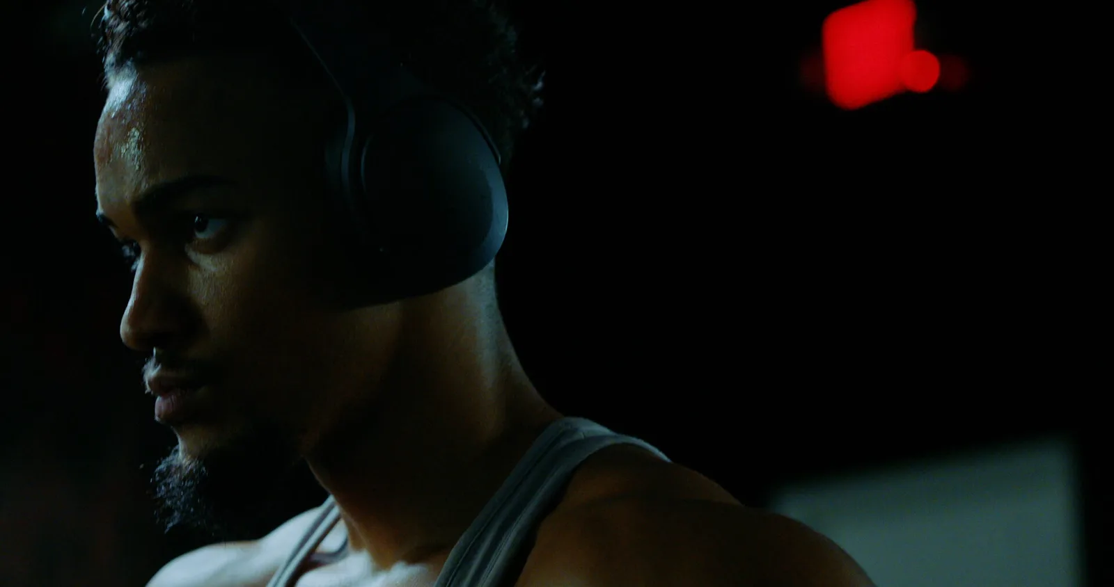 Profile in headphones against black, red practical light in frame