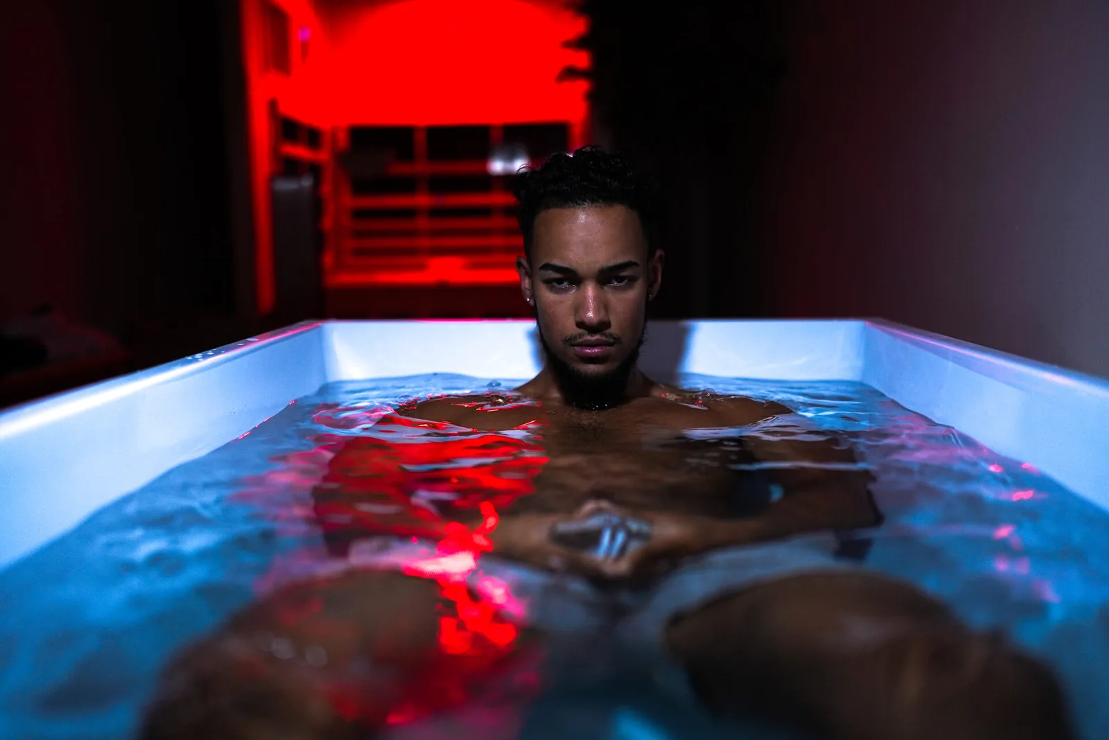 Athlete in an ice bath, lit cold blue from below and red from behind