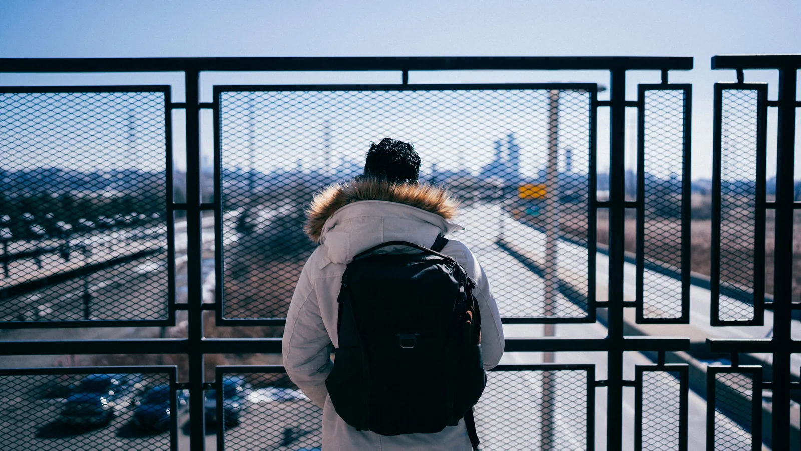 Subject with a backpack on a city overpass, skyline behind