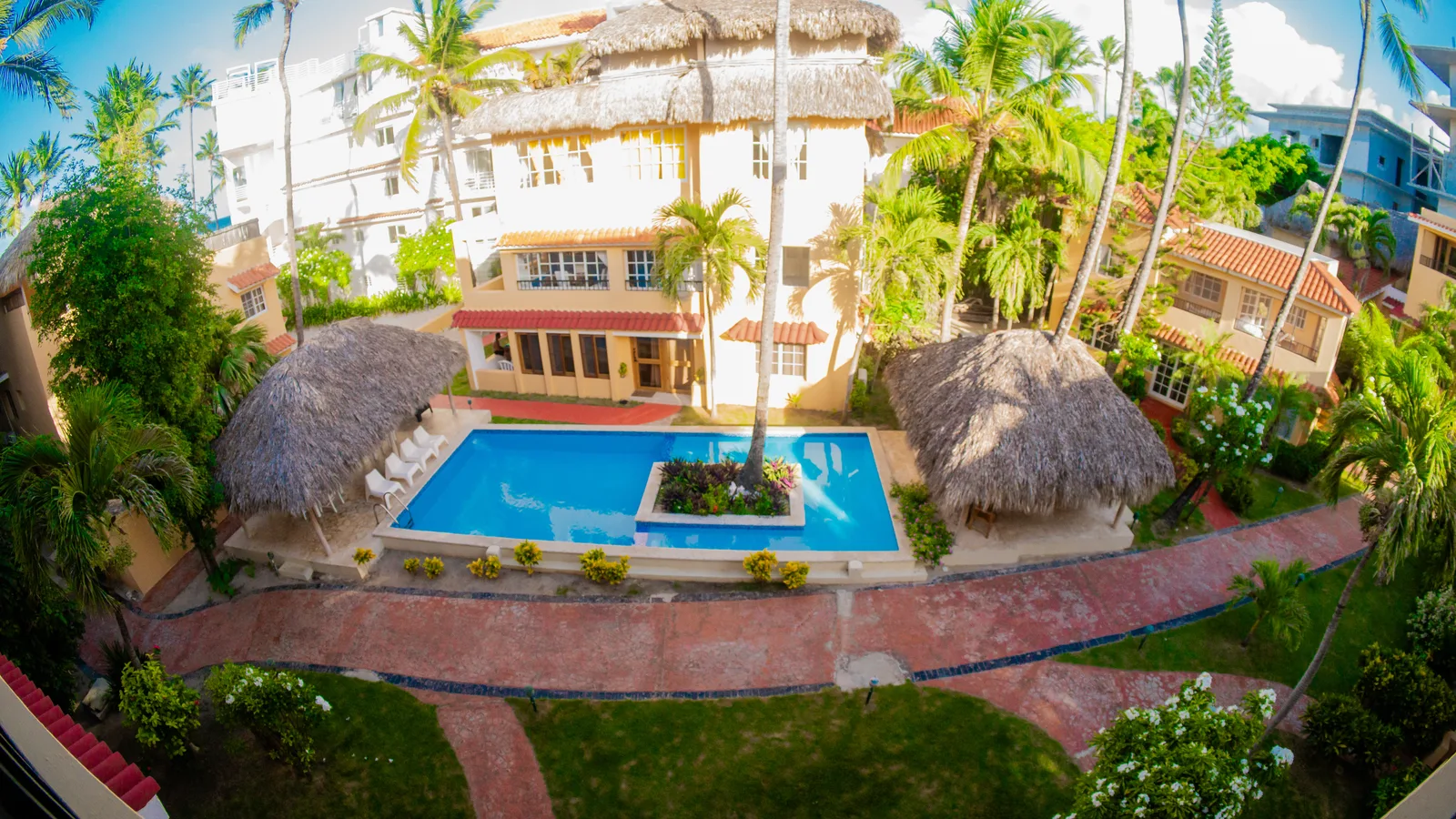 Aerial view of a resort with a pool and palm-thatched cabanas